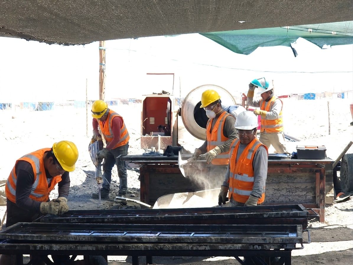 Equipo de operarios con casco y chaleco trabaja en los moldes de placas, junto a la mezcladora