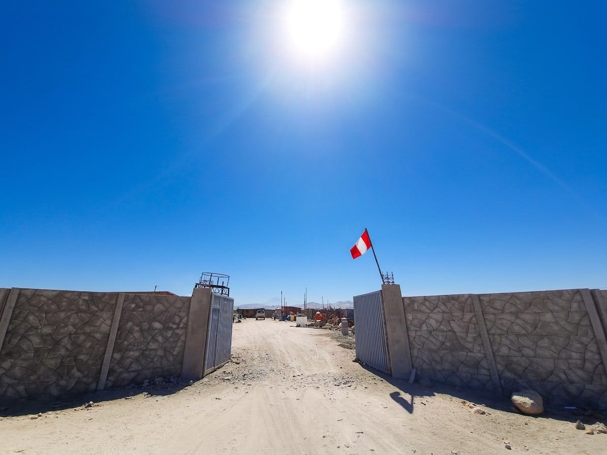 Acceso entre dos tramos de cerco premium con portón metálico y la bandera del Perú