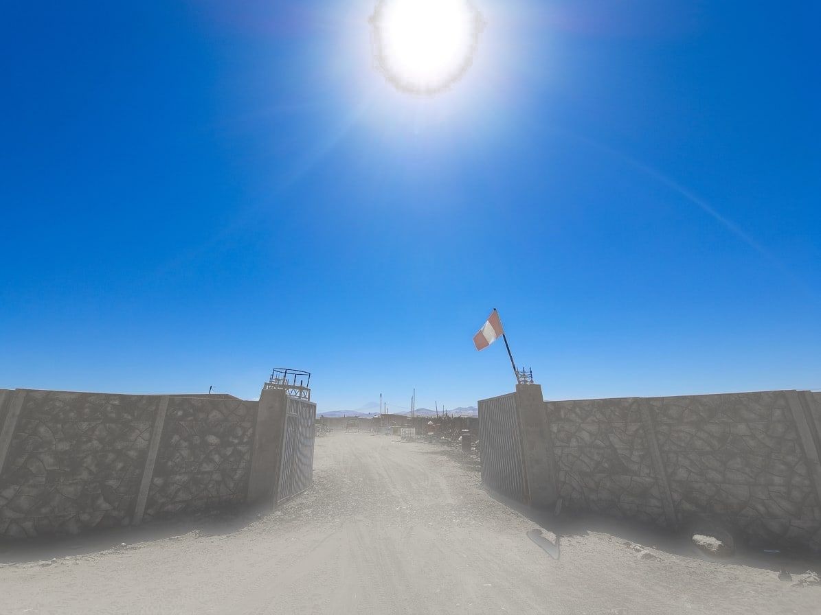 Acceso entre dos tramos de cerco premium con portón metálico y la bandera del Perú