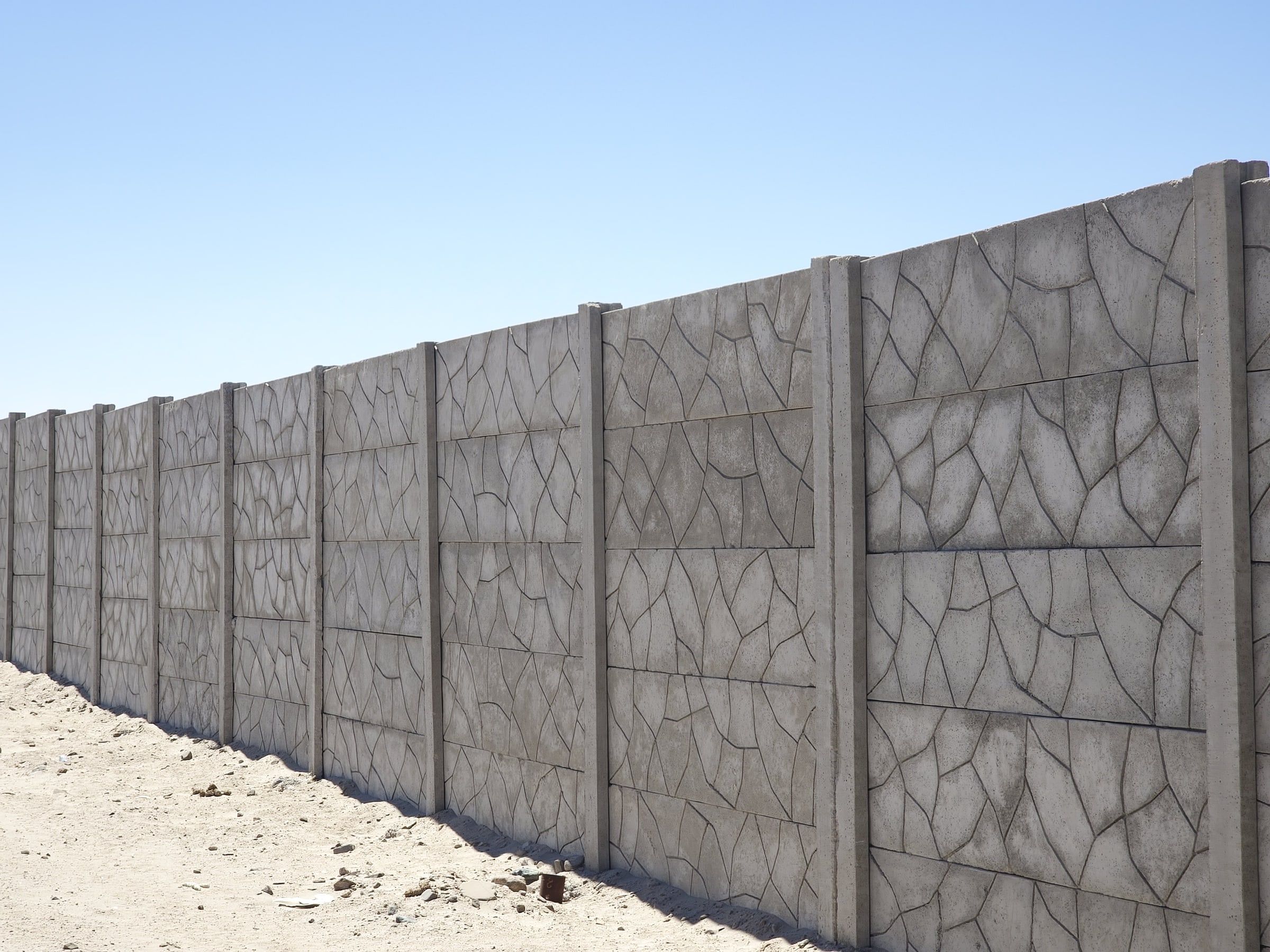 Cerco perimétrico premium de concreto con diseño piedra laja, de varios tramos, bajo cielo despejado